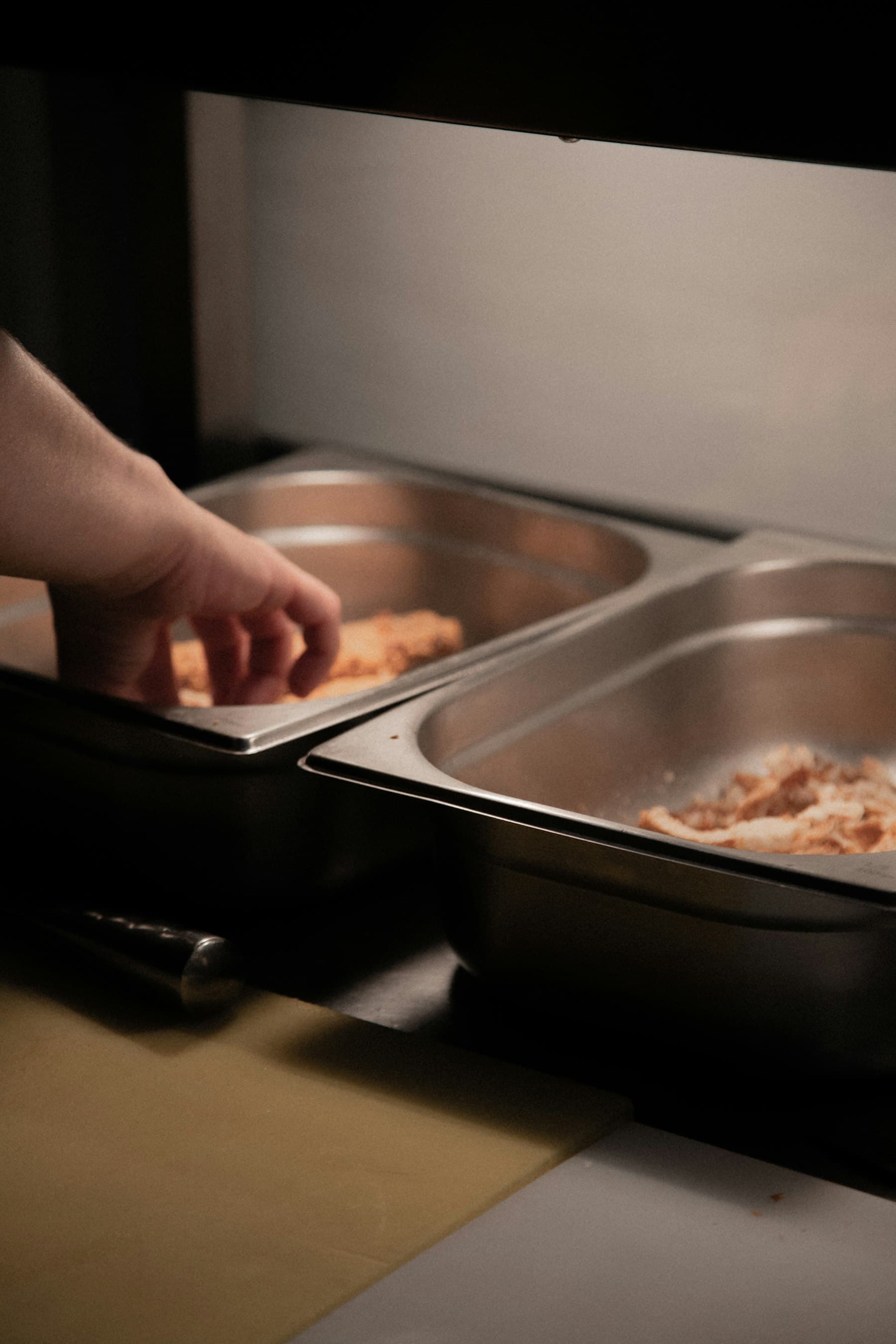 Hands breading fresh chicken tenders in a steel tray